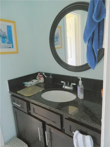 Dark-toned vanity featuring a stone countertop, undermount sink, dual-handle metal faucet, and an oval mirror with a decorative frame