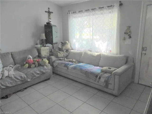 Living area featuring neutral-toned tile flooring, light-colored walls, and a large window with an attached curtain rod