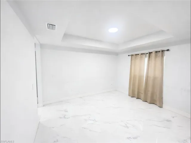 Unfurnished room with light marble finish flooring and a raised ceiling