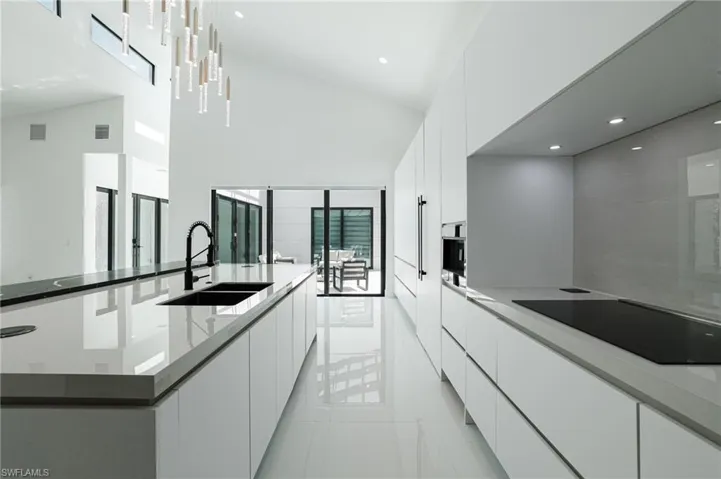 Kitchen with modern cabinets, white cabinetry, black appliances, a spacious island, and light stone countertops