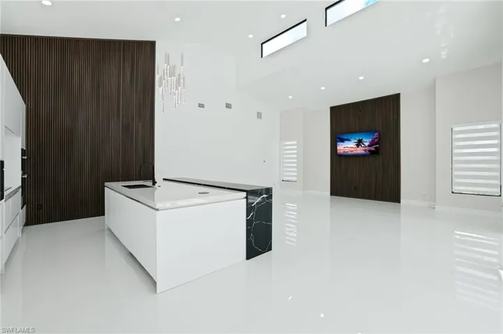 Kitchen with modern cabinets, a kitchen island with sink, white cabinets, light stone countertops, and recessed lighting
