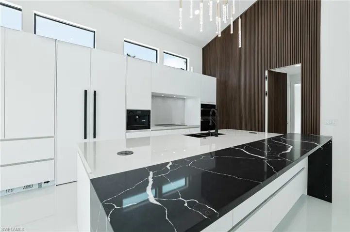Kitchen with modern cabinets, white cabinets, dark stone countertops, wood walls, and a towering ceiling