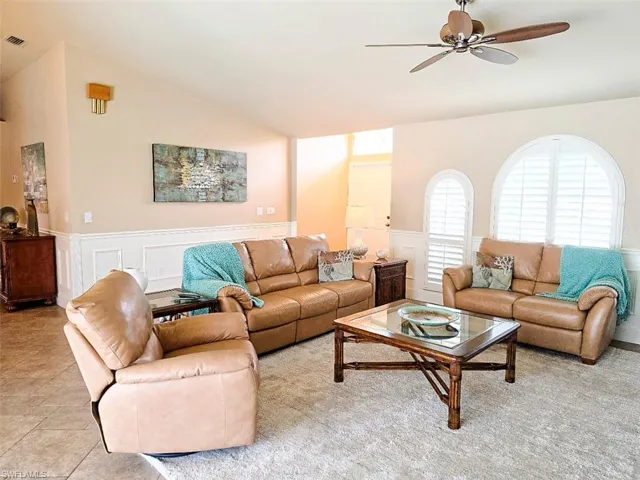 Vaulted ceiling with a ceiling fan, arched windows with plantation shutters, wainscoting, and tile flooring