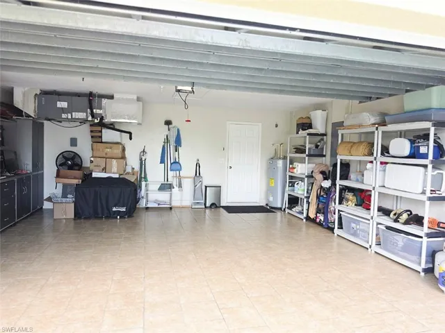 Spacious garage with light-toned tiled flooring, exposed ceiling joists, built-in cabinetry, and a water heater