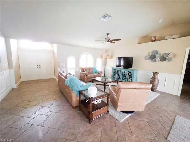 Vaulted ceiling, ceiling fan, arched windows, wainscoting, and tile flooring