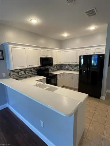 Kitchen featuring kitchen peninsula, white cabinetry, and black appliances