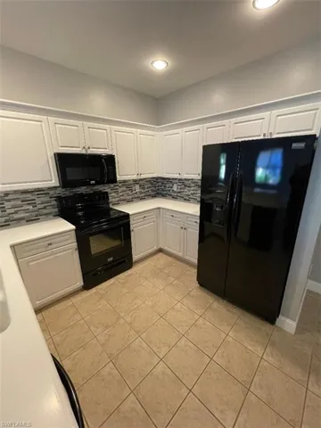 Kitchen featuring decorative backsplash, white cabinets, black appliances, and light tile patterned floors