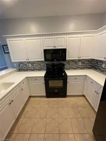 Kitchen featuring decorative tile backsplash, white cabinets, and black appliances