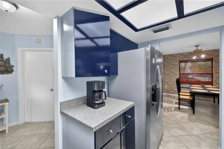 Kitchen with light countertops, blue cabinetry, stainless steel fridge, and light tile patterned floors