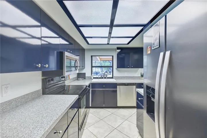 Kitchen with stainless steel appliances, light tile patterned flooring, light stone counters, and blue cabinetry