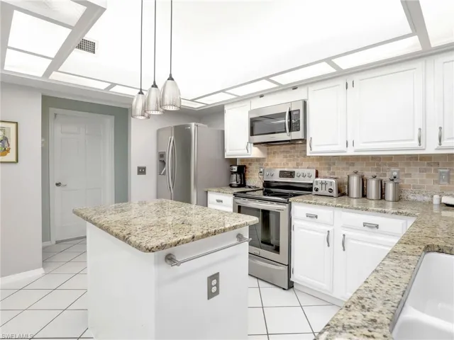 Kitchen with a kitchen island, stainless steel appliances, decorative light fixtures, tasteful backsplash, and light tile floors