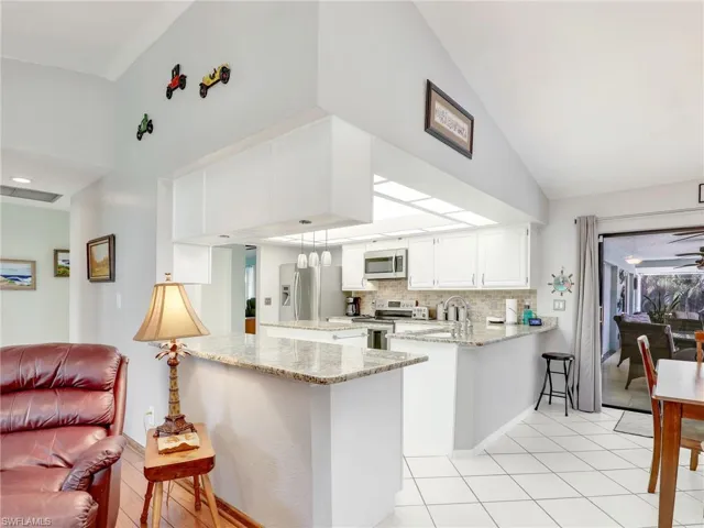 Kitchen with light stone countertops, kitchen peninsula, tasteful backsplash, white cabinets, and appliances with stainless steel finishes