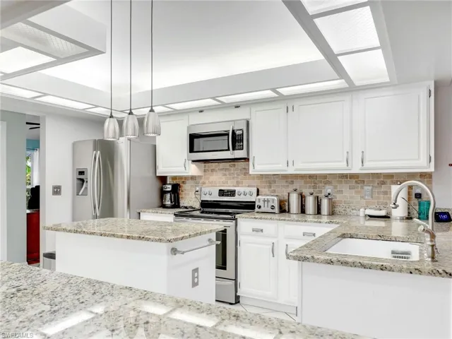 Kitchen with white cabinetry, granite countertops, stainless steel appliances, backsplash, and sink
