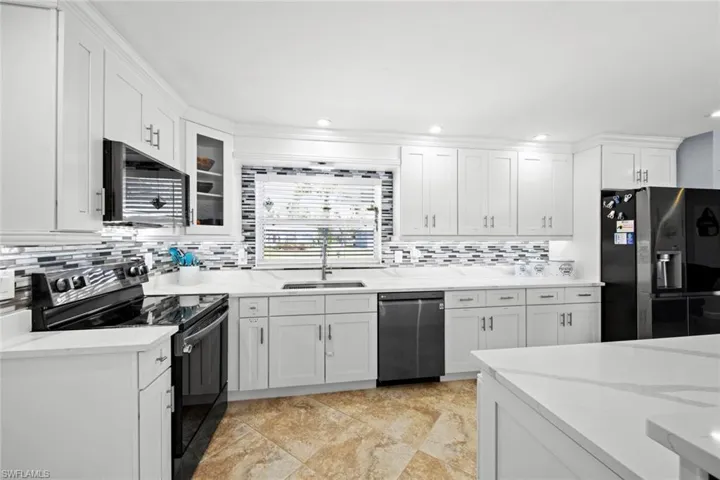 Kitchen featuring a sink, white cabinets, light stone countertops, black appliances, and decorative backsplash