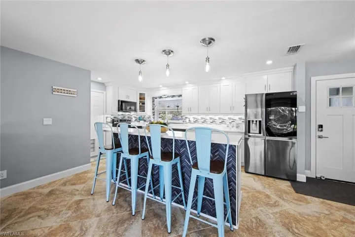 Kitchen featuring a kitchen bar, stainless steel appliances, a center island, decorative backsplash, and visible vents