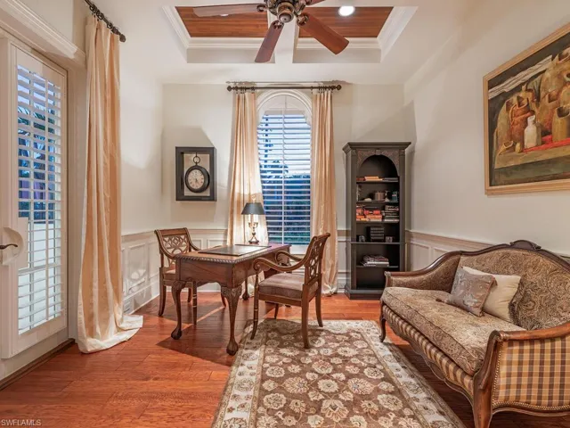 Office area featuring light wood-style flooring, ornamental molding, a ceiling fan, wainscoting, and a raised ceiling