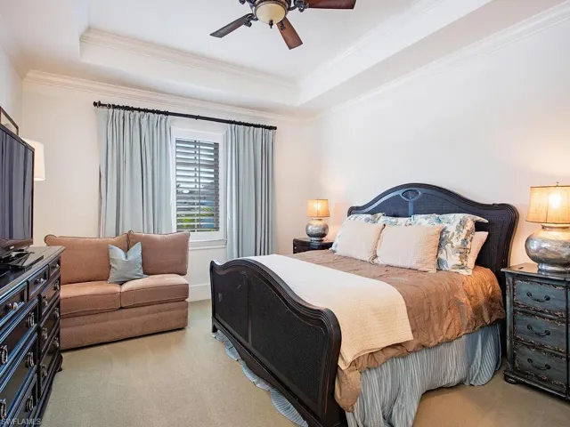 Carpeted bedroom with a raised ceiling, ceiling fan, and crown molding