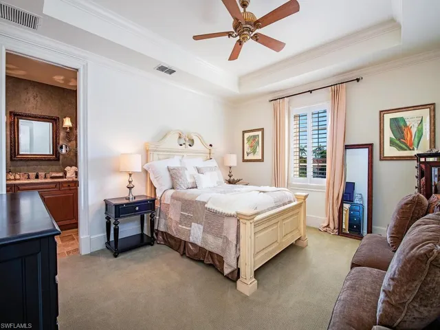 Carpeted bedroom with a raised ceiling, crown molding, ceiling fan, and ensuite bathroom