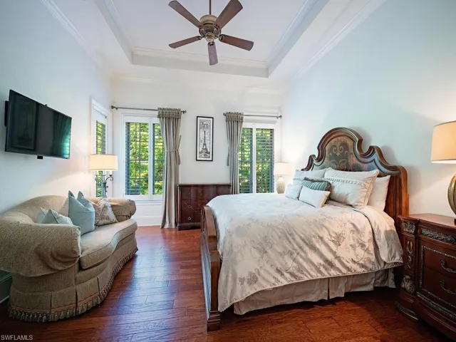 Bedroom featuring hardwood / wood-style flooring, a raised ceiling, crown molding, and ceiling fan