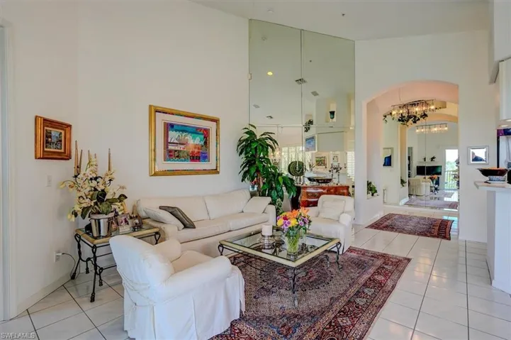 Living room with high vaulted ceiling, light tile patterned floors, arched walkways, an inviting chandelier