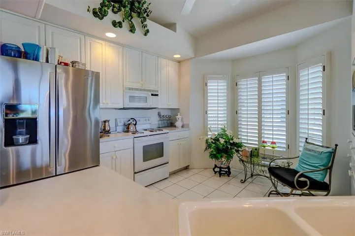 Kitchen with light  cabinets, light countertops, a ceiling fan, light tile patterned floors, and white appliances