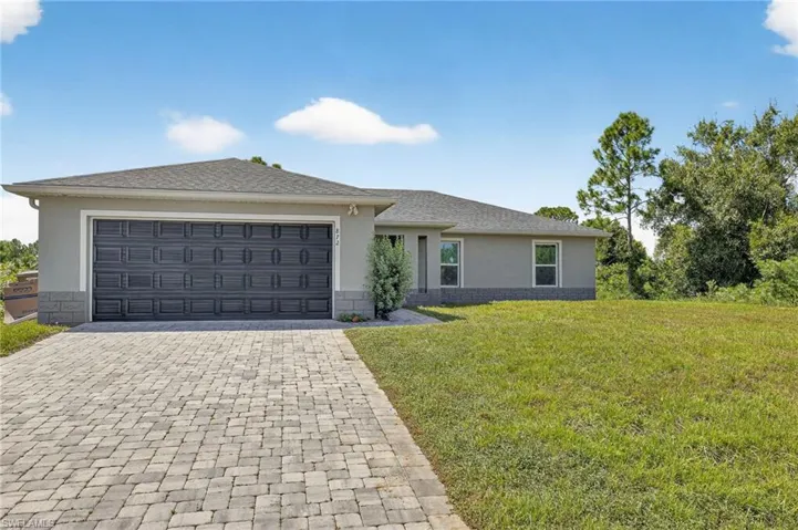View of front of home with stucco siding, decorative driveway, a front yard, an attached garage, and roof with shingles