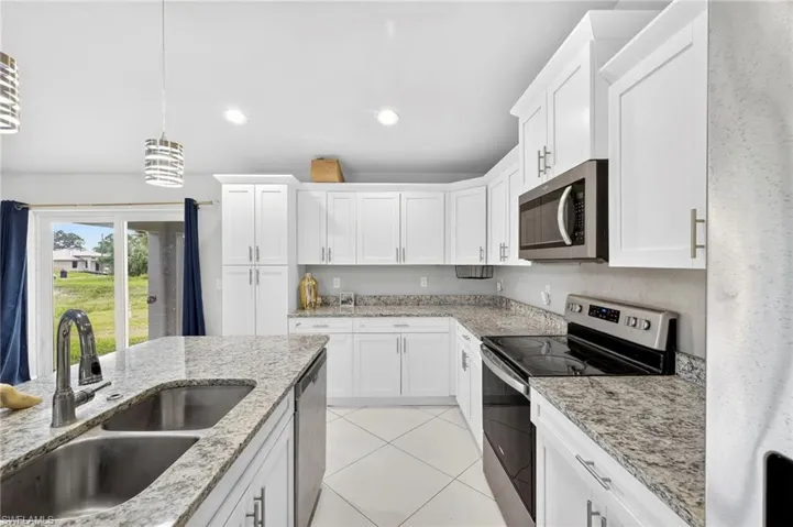 Kitchen featuring appliances with stainless steel finishes, pendant lighting, white cabinetry, light tile patterned floors, and light stone counters