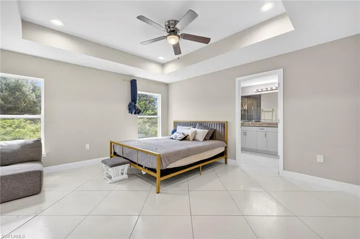 Bedroom with a tray ceiling, light tile patterned floors, ceiling fan, and connected bathroom