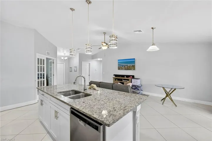 Kitchen featuring white cabinets, light stone counters, ceiling fan, stainless steel dishwasher, and light tile patterned flooring