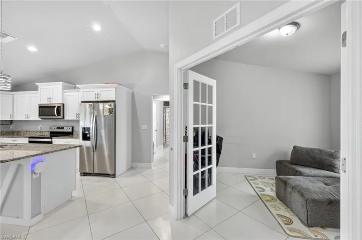 Kitchen featuring dark stone counters, white cabinetry, appliances with stainless steel finishes, vaulted ceiling, and light tile patterned flooring