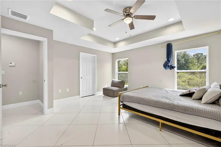 Bedroom with a tray ceiling, light tile patterned floors, a ceiling fan, and recessed lighting