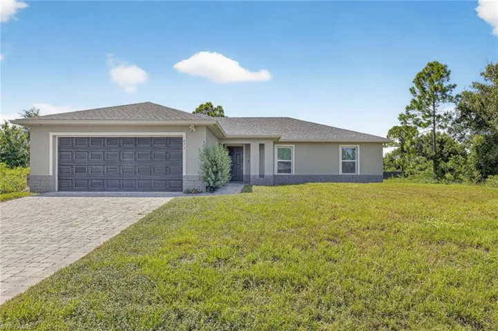 View of front of property featuring stucco siding, a front yard, decorative driveway, a garage, and roof with shingles