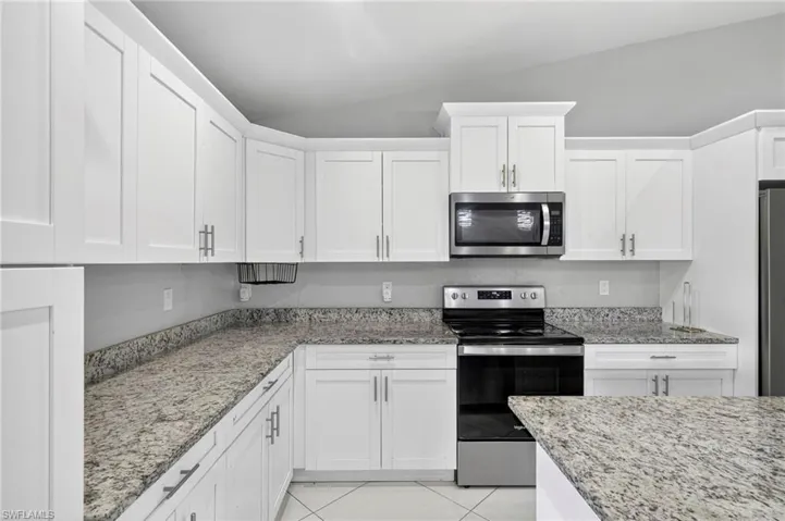 Kitchen with appliances with stainless steel finishes, white cabinets, light tile patterned flooring, and vaulted ceiling