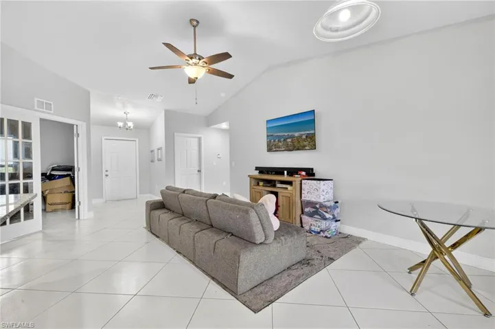 Living room with lofted ceiling, light tile patterned floors, a ceiling fan, and a chandelier