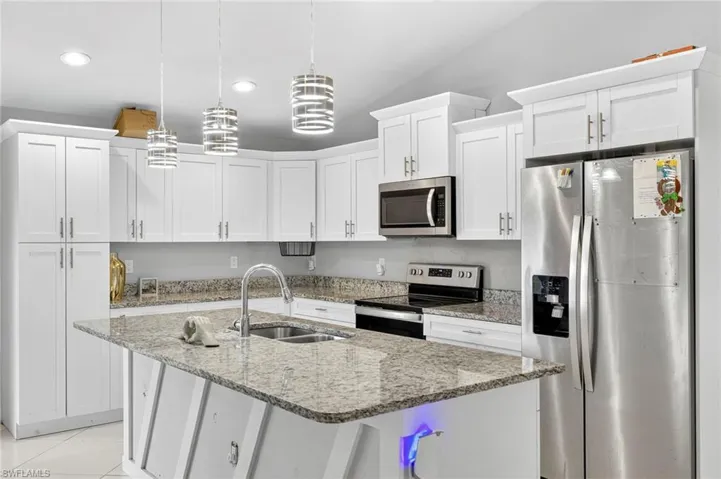 Kitchen featuring stainless steel appliances, white cabinets, decorative light fixtures, light stone countertops, and a kitchen island with sink