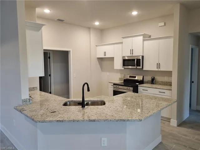 Kitchen featuring a peninsula, appliances with stainless steel finishes, light stone counters, white cabinets, and recessed lighting