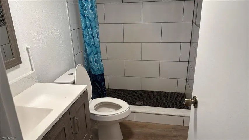 Full bath with a textured wall, vanity, a stall shower, and wood finished floors