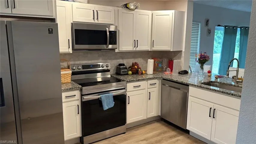 Kitchen featuring appliances with stainless steel finishes, dark stone counters, white cabinets, light wood-style floors, and a textured ceiling