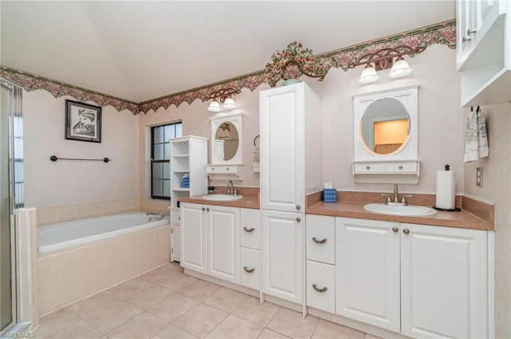 Bathroom featuring two vanities, a bath, lofted ceiling, light tile patterned floors, and a stall shower