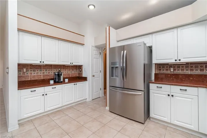 Kitchen featuring stainless steel fridge, backsplash, white cabinetry, and light tile patterned floors