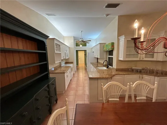 Kitchen featuring light stone counters, white appliances, white cabinets, light tile patterned floors, and a chandelier