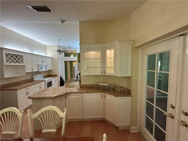 Kitchen with glass insert cabinets, white appliances, white cabinetry, dark stone countertops, and light tile patterned flooring