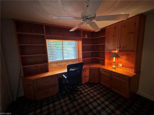 Unfurnished office with built in study area, ceiling fan, and dark colored carpet
