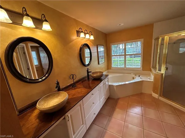 Full bathroom with double vanity, light tile patterned floors, a bath, a stall shower, and a textured wall