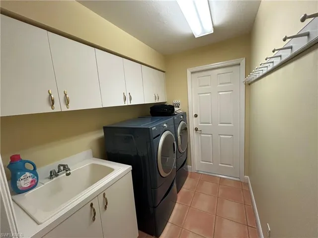 Washroom with light tile patterned floors, washing machine and clothes dryer, and cabinet space