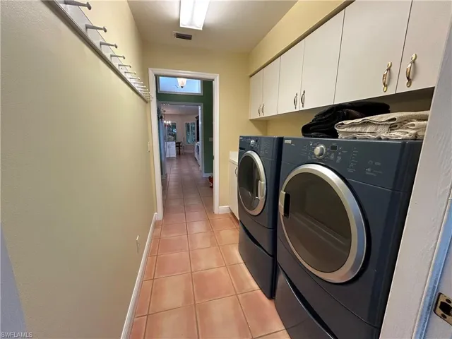 Washroom with light tile patterned flooring, cabinet space, and washer and clothes dryer