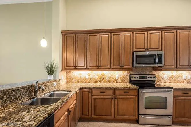 Kitchen with dark stone countertops, appliances with stainless steel finishes, decorative backsplash, and a sink