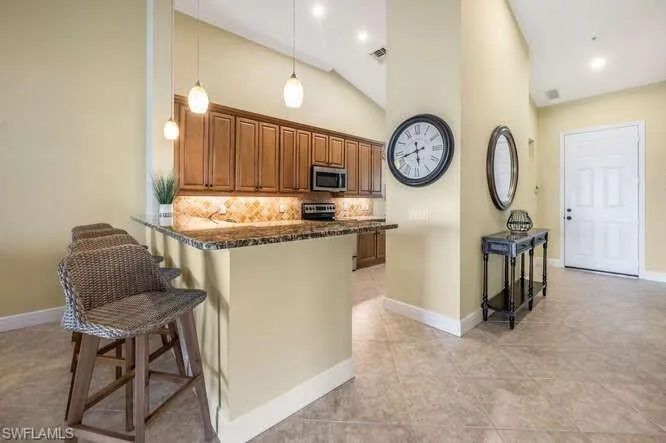 Kitchen featuring brown cabinets, stainless steel appliances, tasteful backsplash, dark stone countertops, and a kitchen breakfast bar