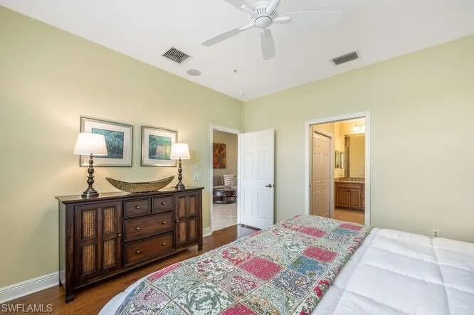 Bedroom featuring baseboards, visible vents, dark wood-type flooring, and connected bathroom