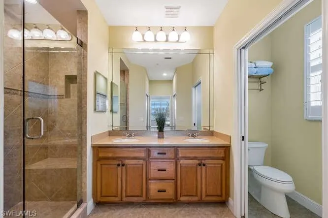 Full bathroom featuring toilet, a shower stall, double vanity, and a sink